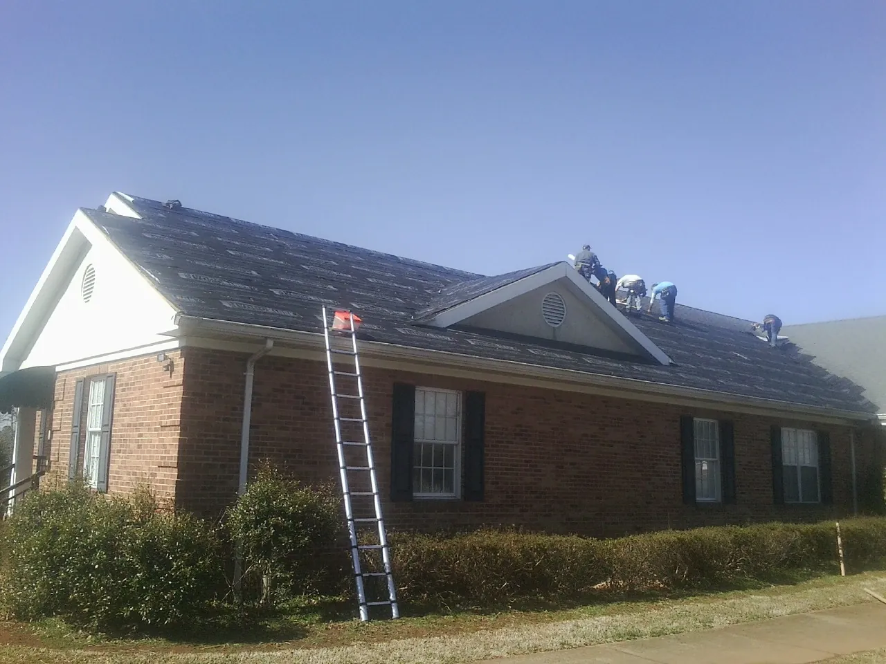 Crew tearing shingles off a brick ranch roof with a ladder set — Emergency Roof Repair work by our crew in Egan
