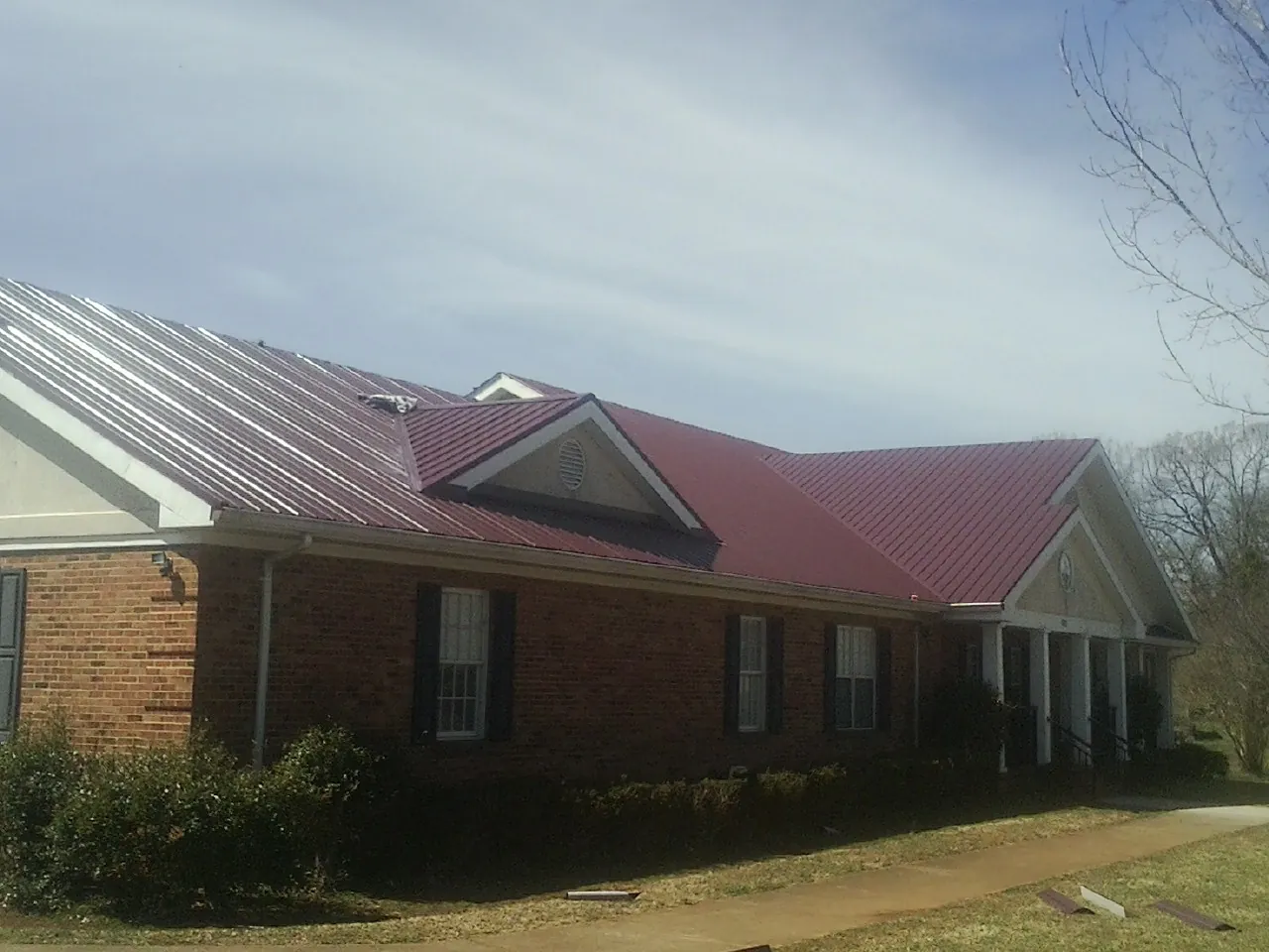 Red metal roof with gabled entries on a long brick building, from a Hail Damage Roof Repair job in Egan