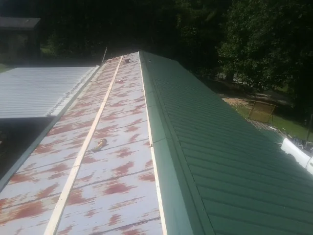 Old rusted panels beside newly installed green metal roofing — Wind Damage Roof Repair by Roofing Brothers in Egan