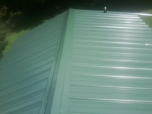 New green metal panels meeting at the ridge of a roof — Flat Roof Repair work by our crew in Egan