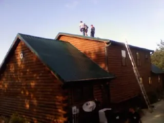 Crew on the ridge of a green metal roof on a two story log home in Egan